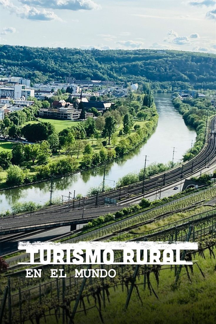 A river running through a green valley, with buildings on one bank and a railway line on the other.