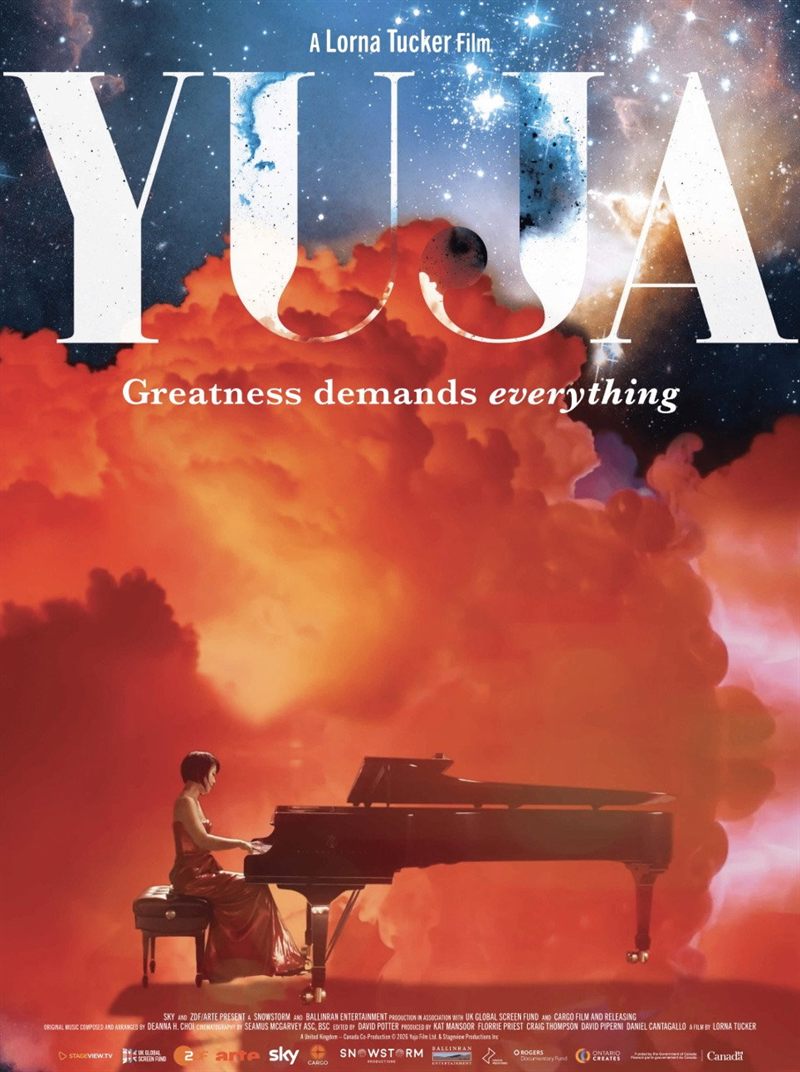 A pianist plays a grand piano amid huge orange clouds.